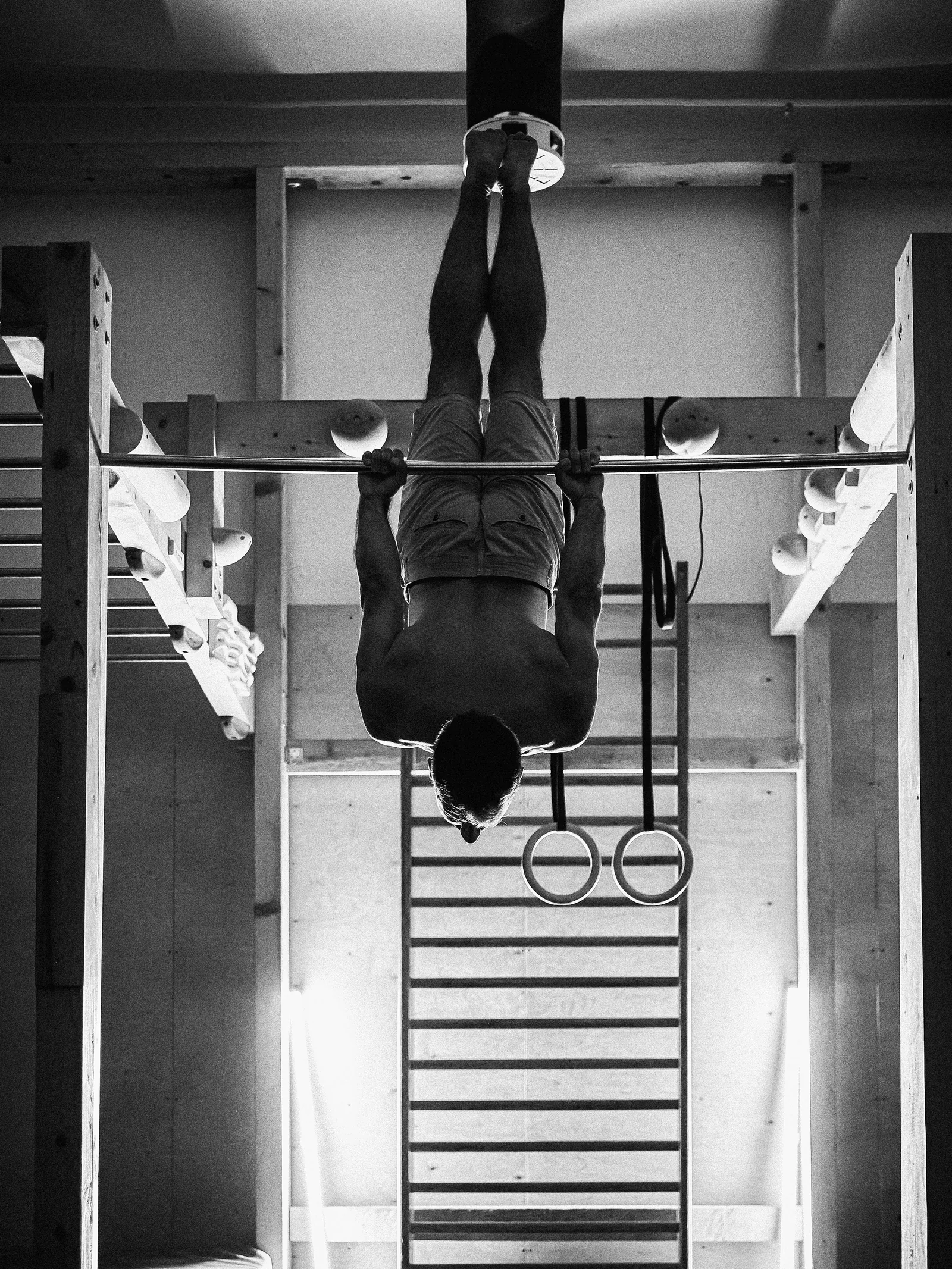Athlete hanging upside down from a bar in a gym, black and white photo by Nikola Ramčević