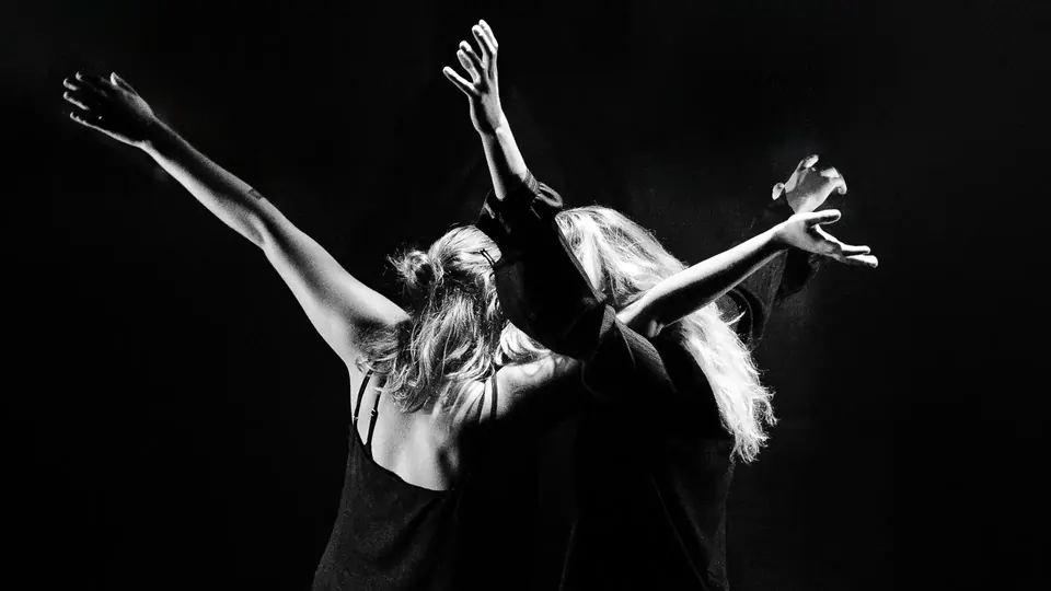 Two dancers with raised arms on a dark stage