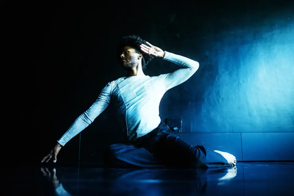 Dancer posing on a reflective floor in blue light